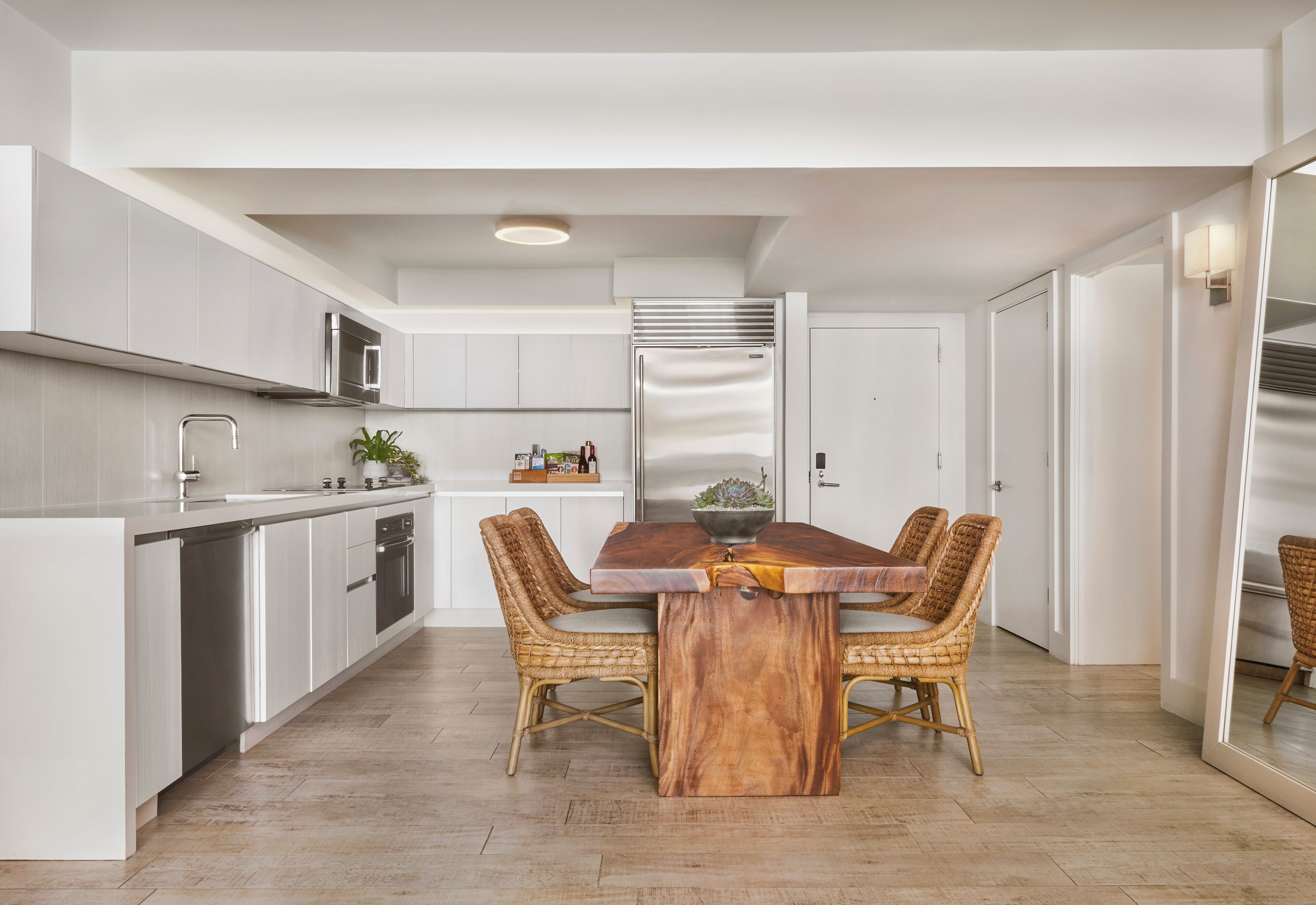 Una cocina moderna con armarios blancos, una mesa de comedor de madera, sillas de mimbre y un horno empotrado.