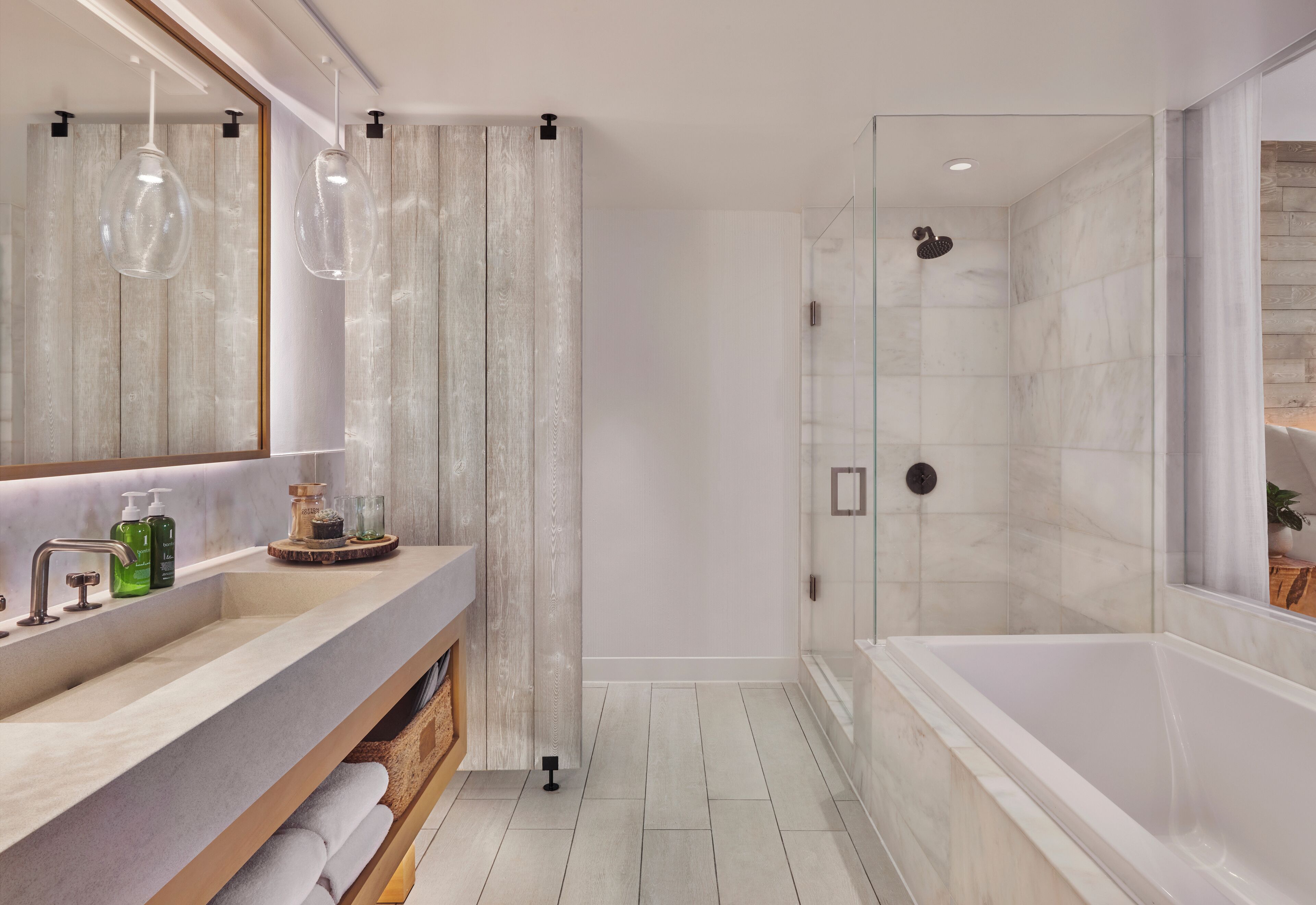 A modern bathroom with a large mirror, two sinks, a shower, and a bathtub.