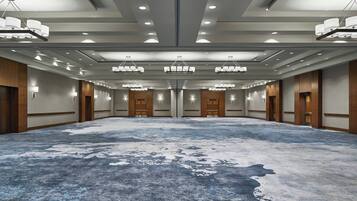 A large, empty conference room with a blue carpet, wooden paneling, and multiple chandeliers.