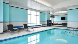Une piscine intérieure dotée de chaises longues et d’un écran de télévision fixé au mur.