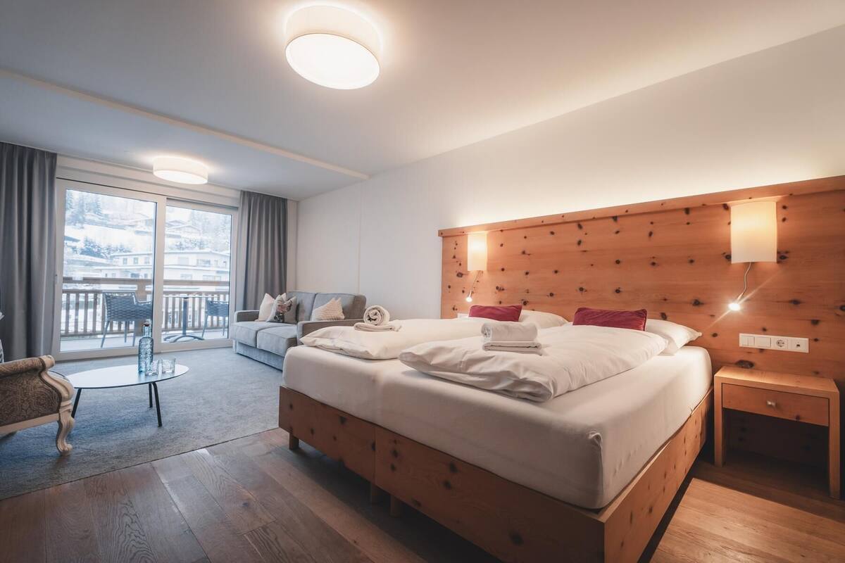 A hotel room with a large bed, a wooden headboard, a bedside table, a chair, and a balcony with a view.