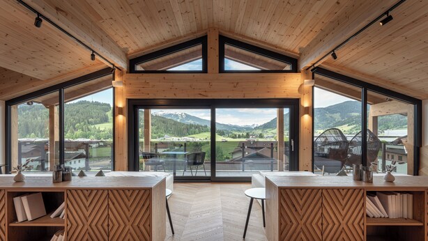 Un intérieur moderne avec des lambris en bois, de grandes fenêtres et une vue sur un paysage montagneux.