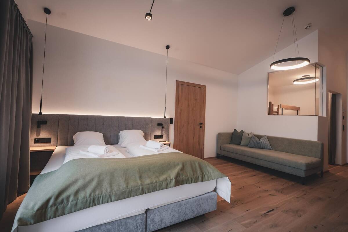 A modern bedroom with a large bed, a sofa, a wooden door, and a mirror.