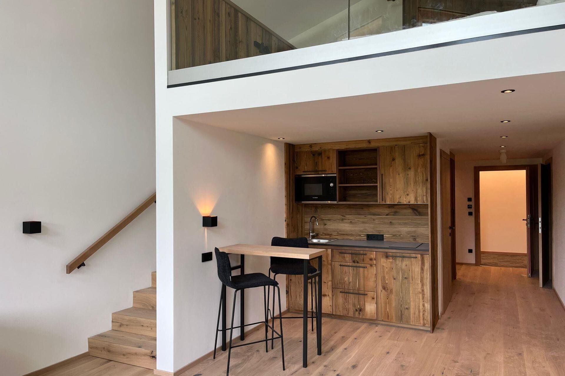 A modern kitchen with wooden cabinetry, a built-in microwave, and a bar area with stools.