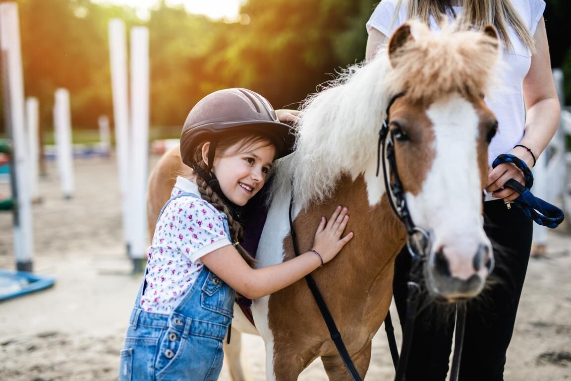 A person in a white shirt and black pants standing next to a horse.