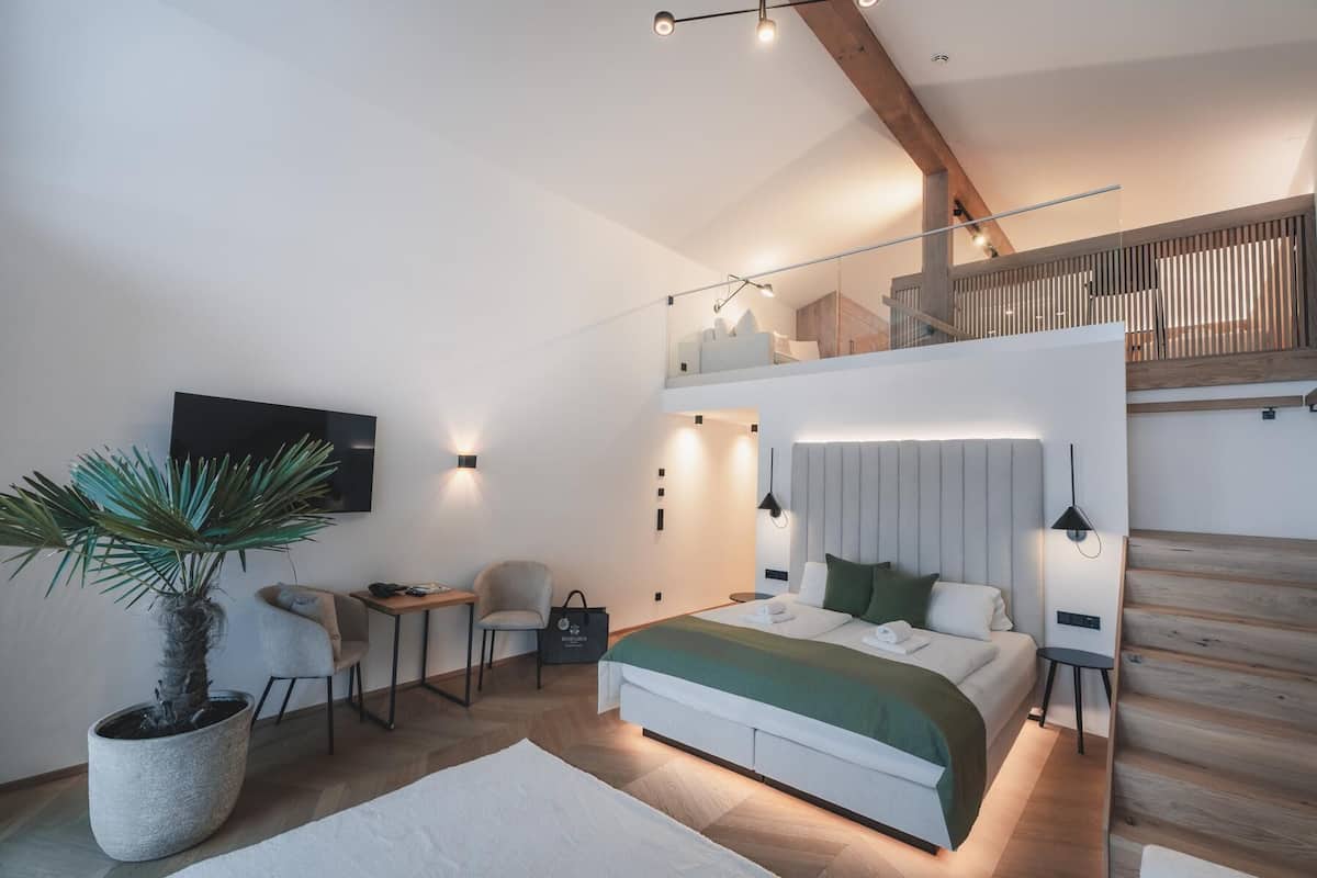 A modern bedroom with a bed, bedside tables, a TV, and a staircase.