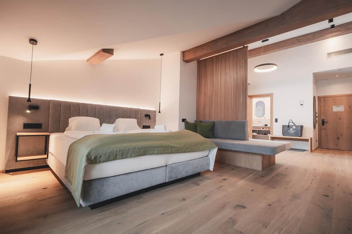 A modern bedroom with a large bed, a bench, a desk, and a bathroom visible through an open door.