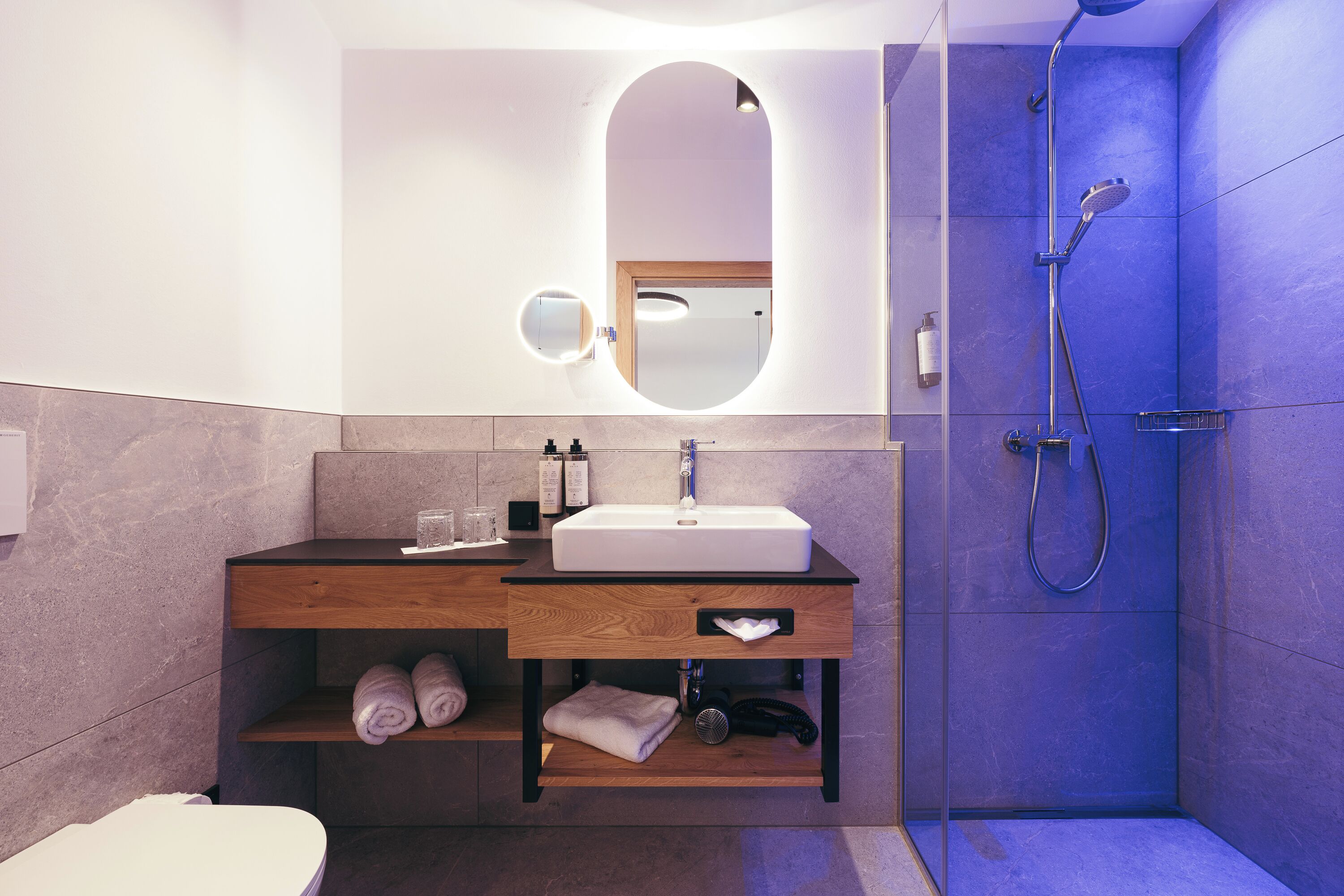 A modern bathroom with a white sink, wooden vanity, a mirror, and a shower enclosure.