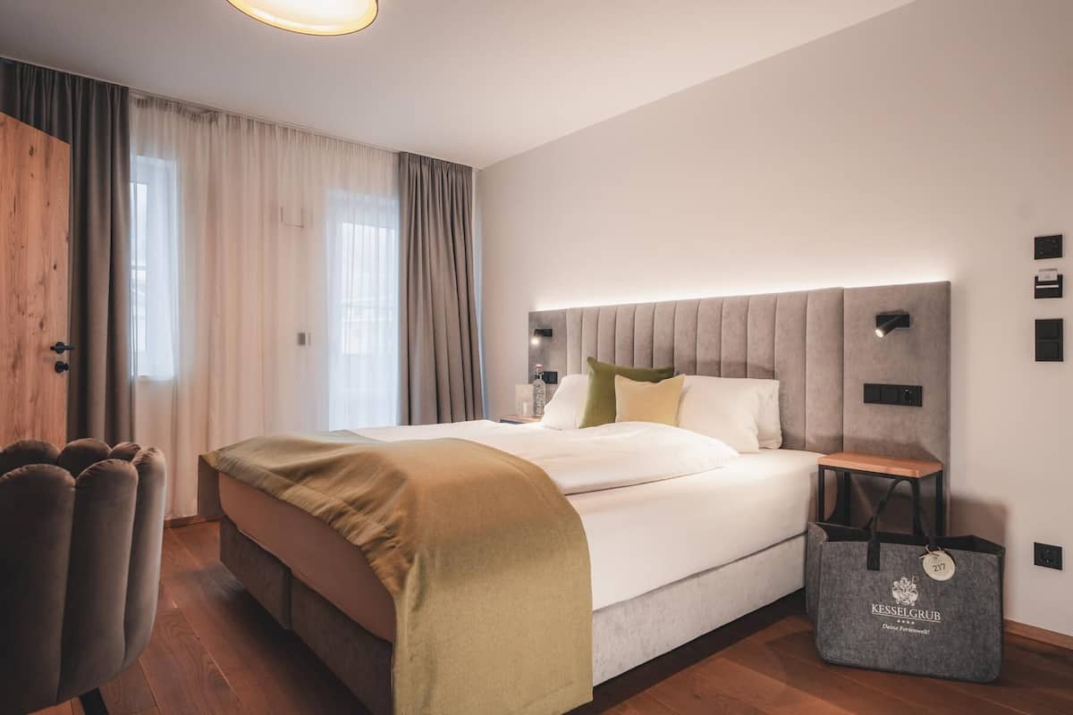 A modern hotel room with a large bed, a wooden wardrobe, a desk, and a nightstand.