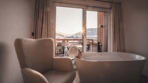 Une pièce dotée d’une grande baignoire, d’un fauteuil moelleux et offrant une vue sur un paysage enneigé par le biais d’une grande fenêtre.