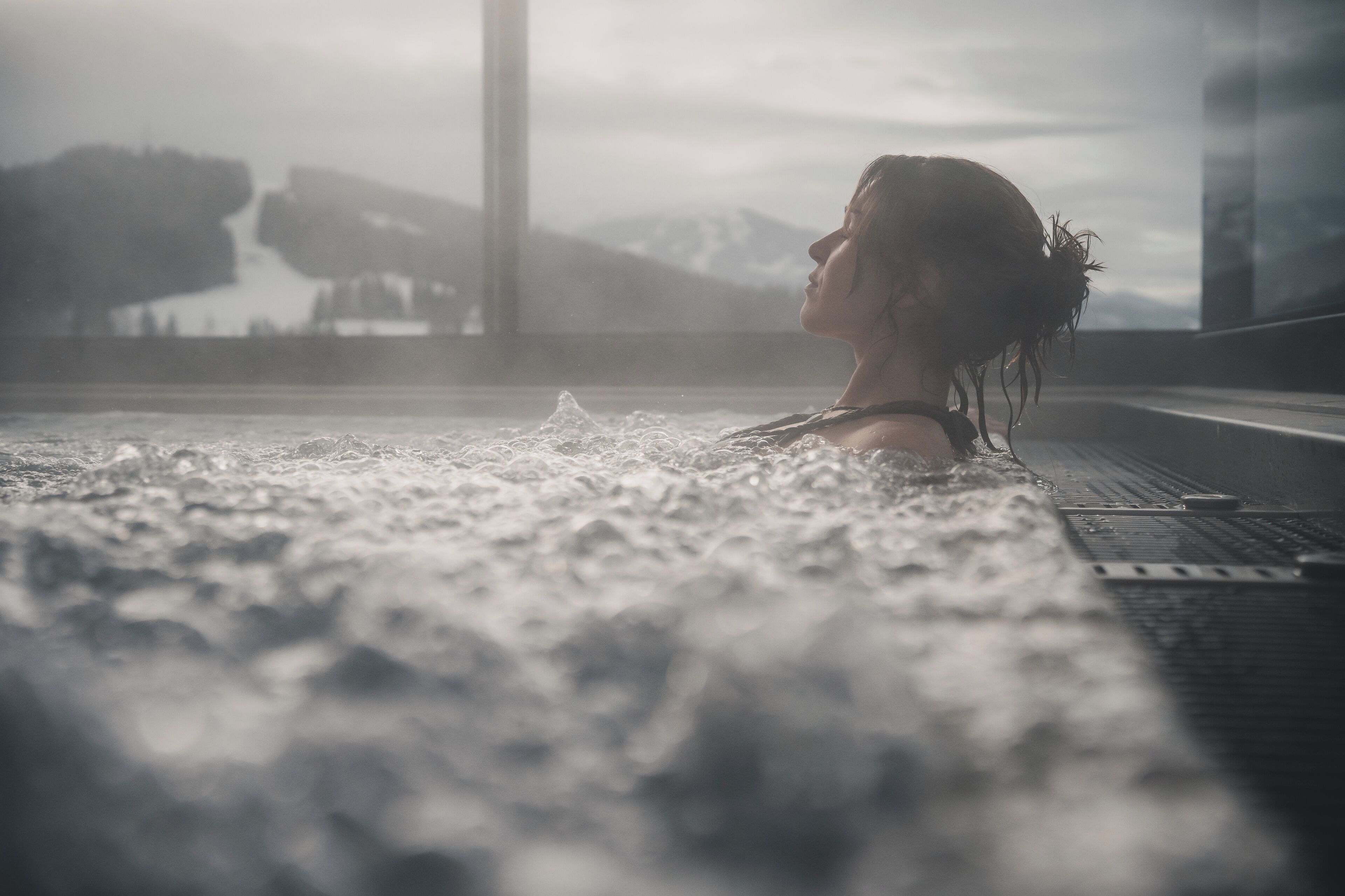 A person in a hot tub with a mountainous landscape in the background.
