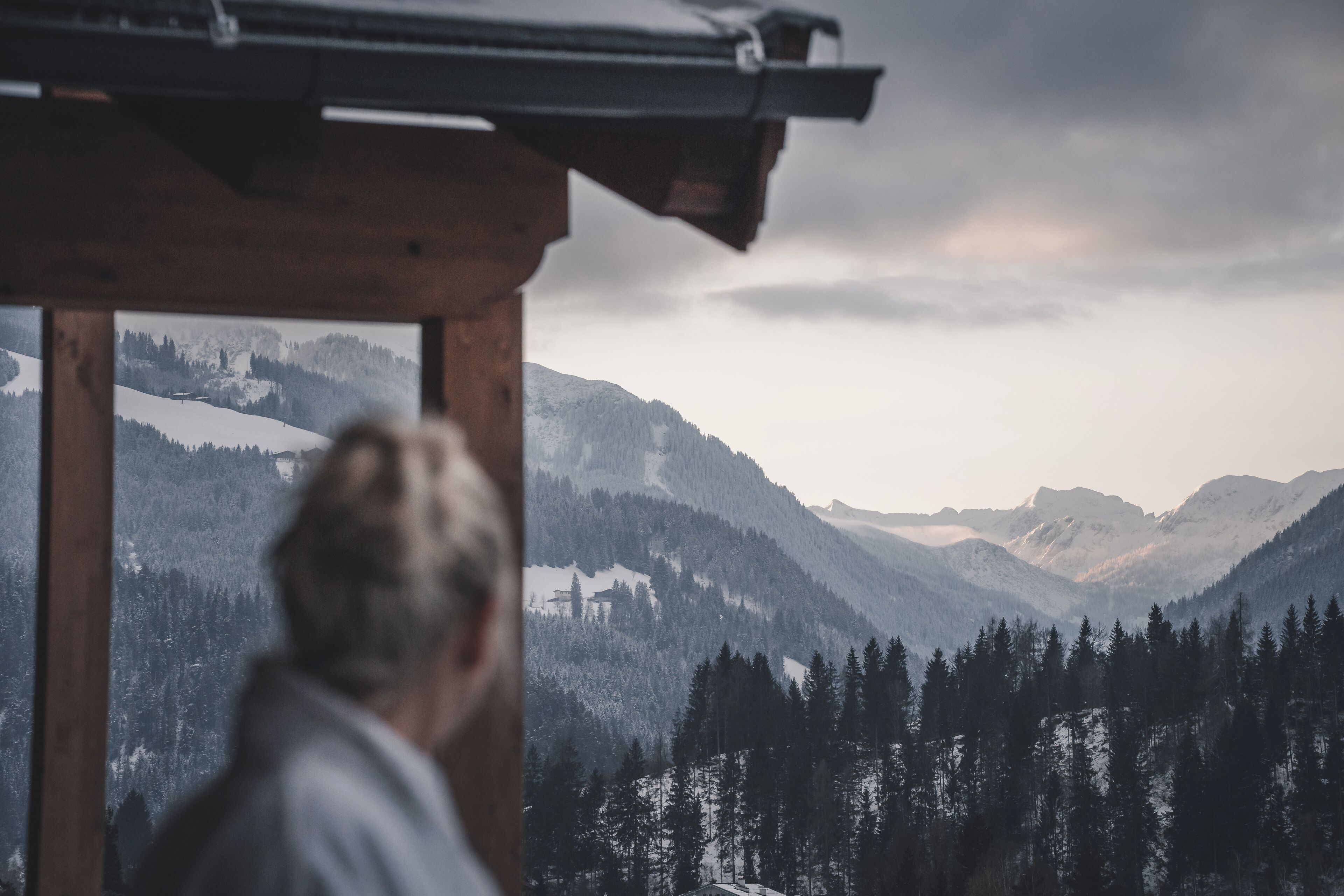 Eine Person blickt aus einem Fenster auf eine gebirgige Landschaft.