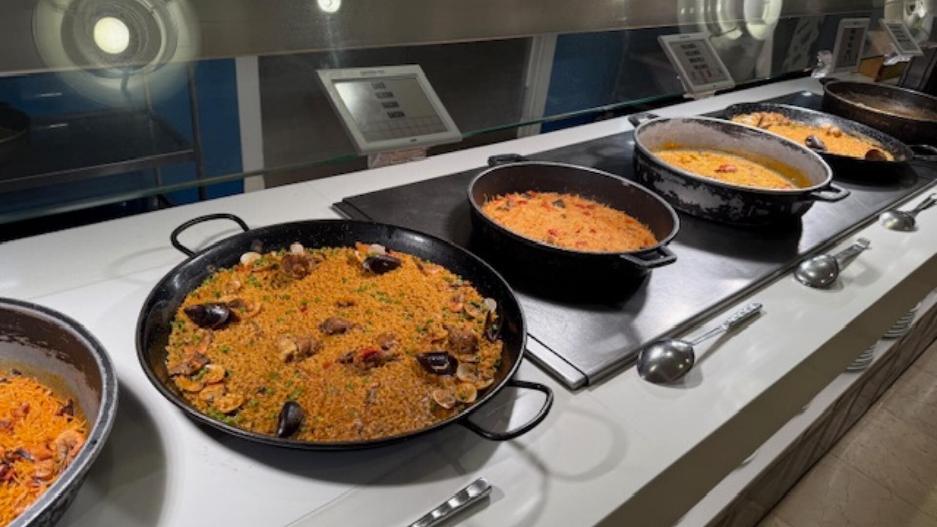 Un bufé con diversos platos, incluyendo una paellera grande de arroz con mariscos.