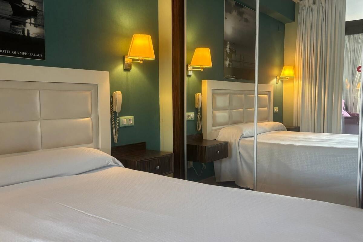 Una habitación de hotel con dos camas, un espejo, lámparas de noche y un teléfono.