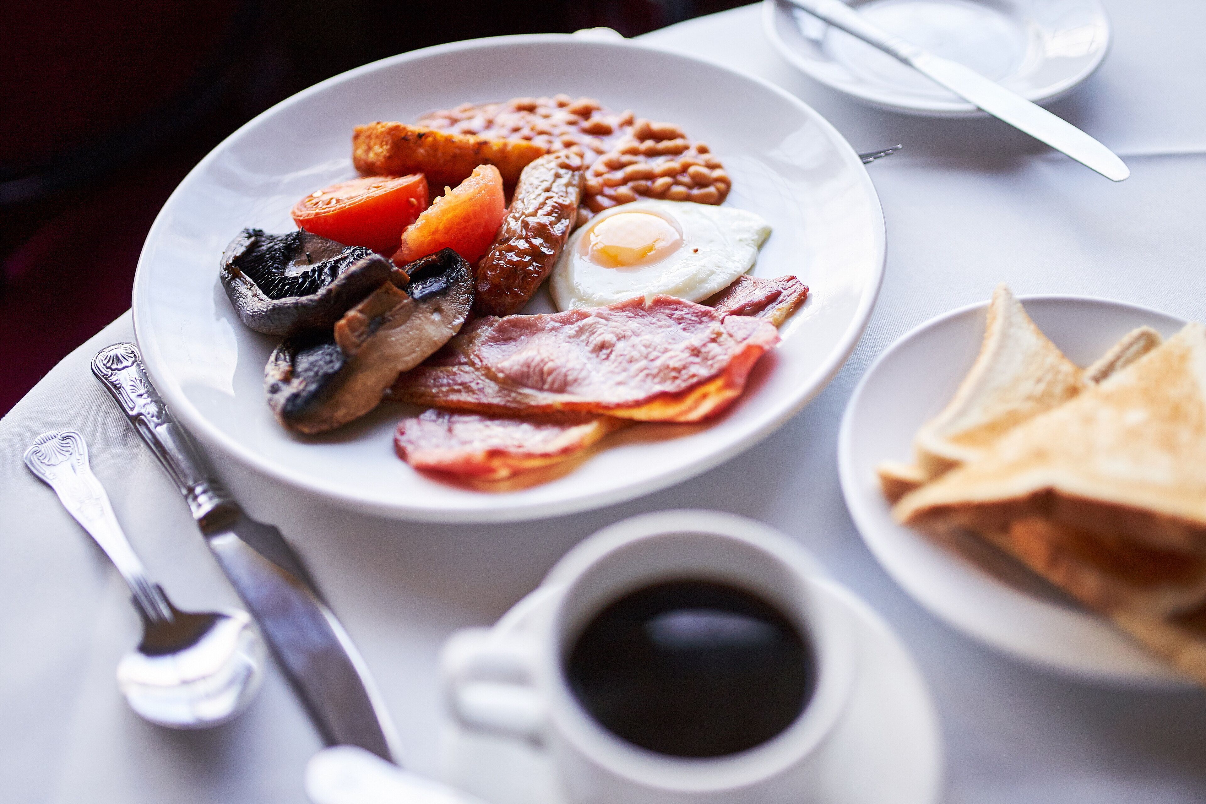 A breakfast plate with eggs, bacon, sausages, beans, mushrooms, and tomatoes.