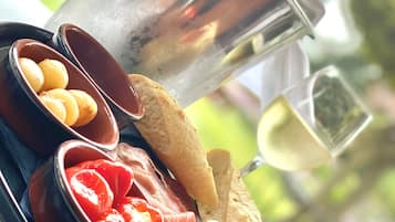 Tabla de formatges i embotits amb olives i pa, acompanyada d'una ampolla de vi blanc.