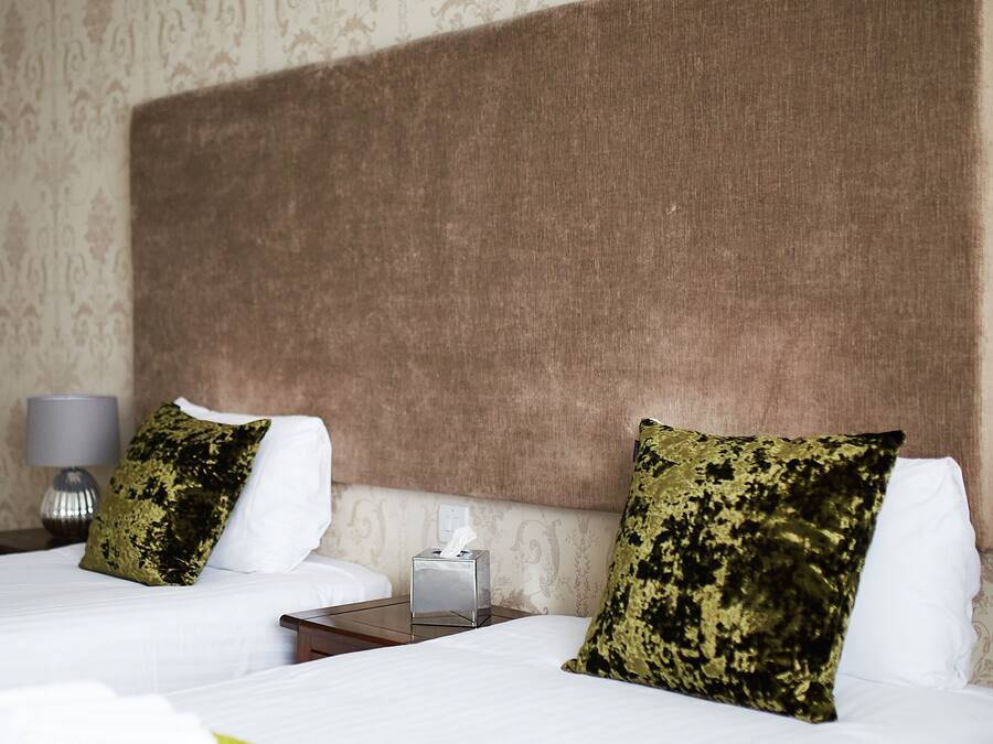 A hotel room with two beds, each with white linens and a single green and black patterned pillow. There is a bedside table with a lamp and a tissue box.