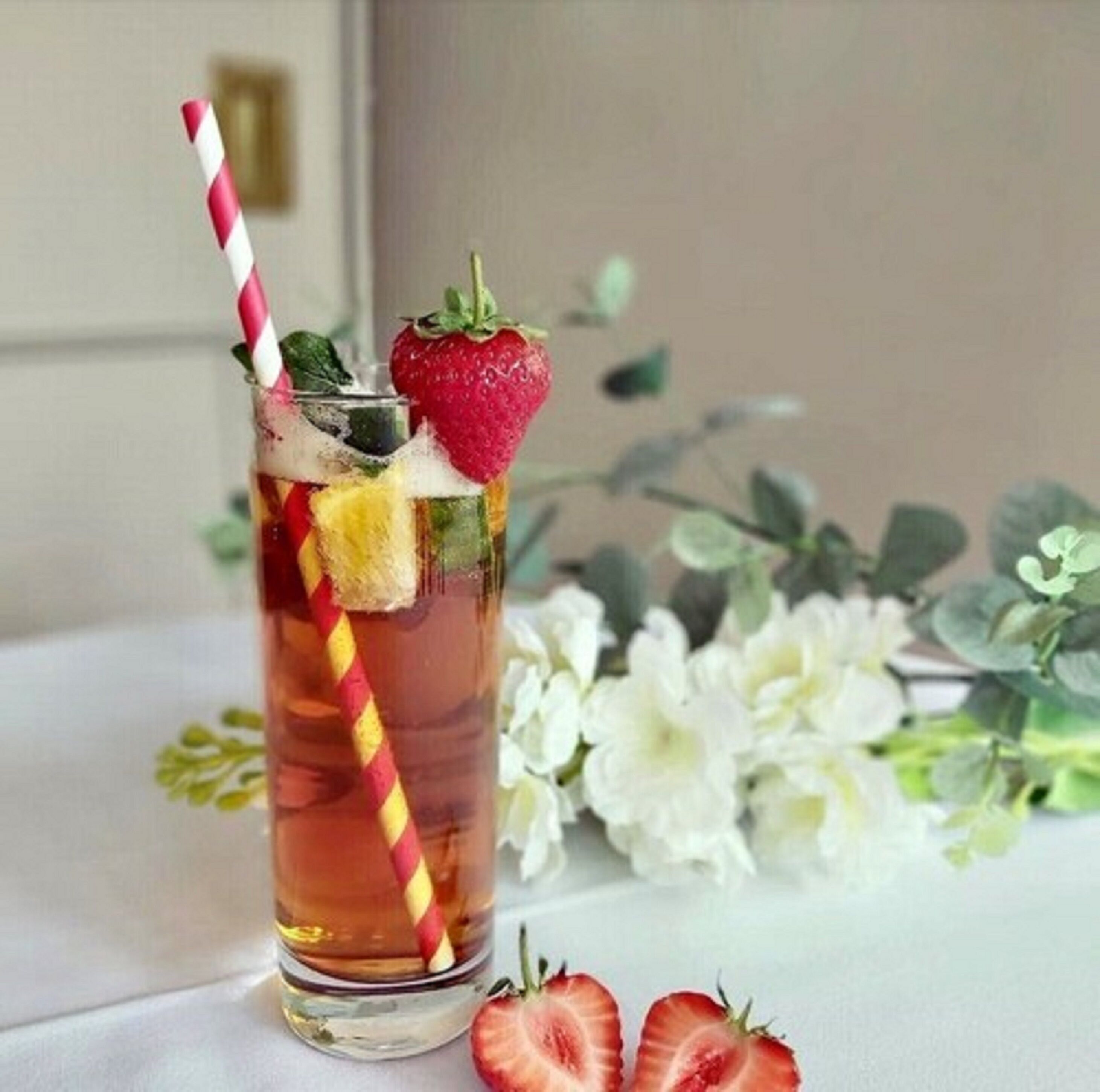 A glass of iced tea with a strawberry and mint garnish, a striped straw, and a slice of lime.