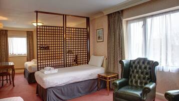 Quarto de hotel com uma cama grande, uma poltrona verde, uma mesa pequena e uma escrivaninha com cadeira.