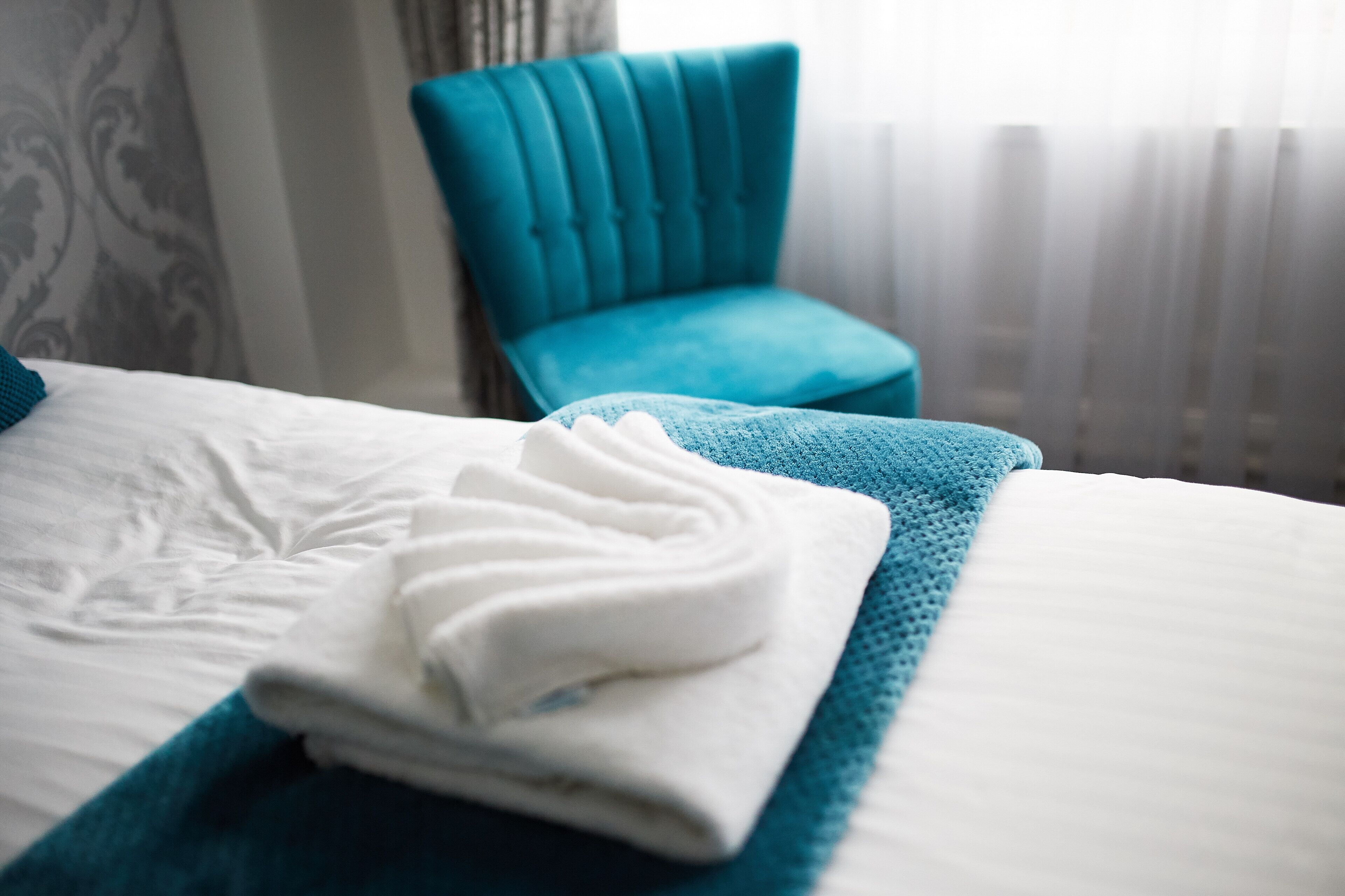 A neatly made bed with a folded white towel and a teal blanket.