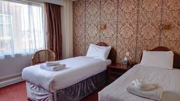 Habitación de hotel con dos camas, una ventana con cortinas, papel tapiz estampado y una silla de madera.