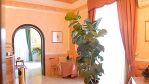 A room with a large potted plant, a dining area with a table and chairs, and a view through an archway to another room. - Hotel Gresi (Catania)
