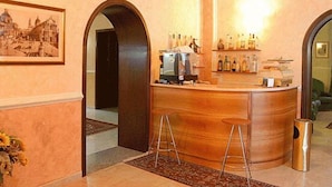 A bar area with a wooden counter, stools, and a coffee machine. There is a framed picture on the wall and a shelf with bottles. - Hotel Gresi (Catania)