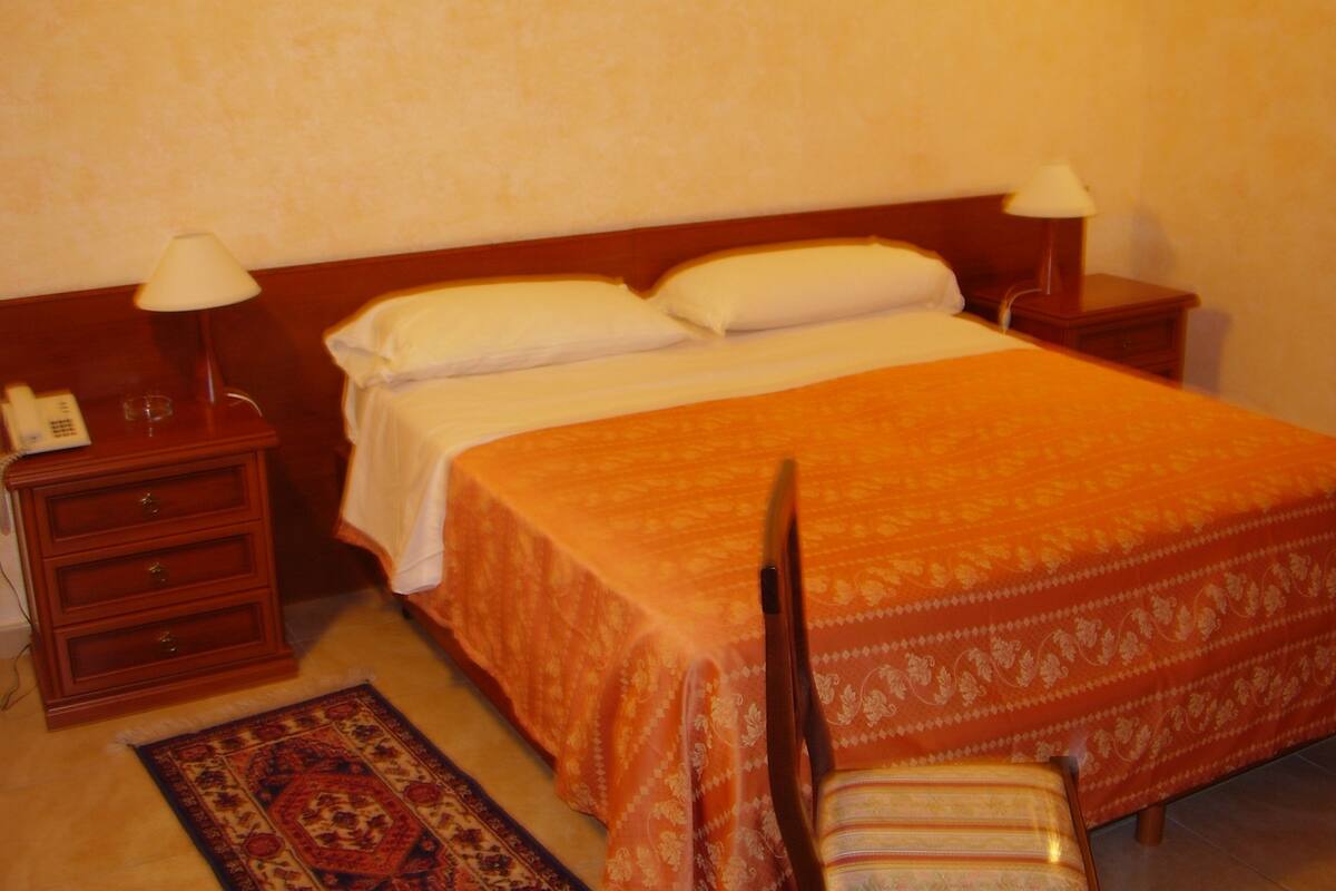 A hotel room with a bed, two bedside tables with lamps, a nightstand, and a chair.