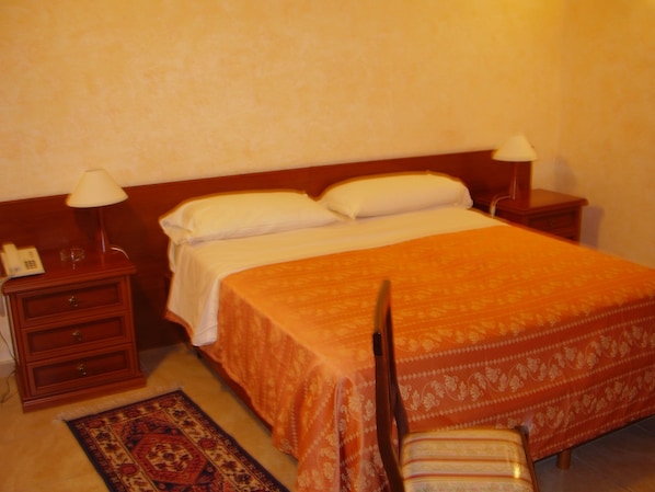 A hotel room with a bed, two bedside tables with lamps, a nightstand, and a chair. - Hotel Gresi (Catania)