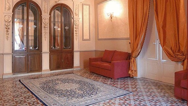A room with a patterned rug, a red sofa, and a large window with orange curtains. - Hotel Gresi (Catania)