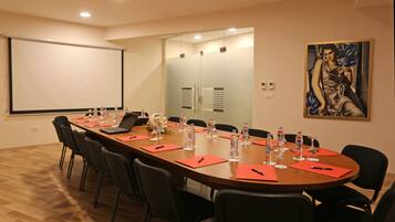 A conference room with a long table, chairs, a projector screen, and a painting on the wall.
