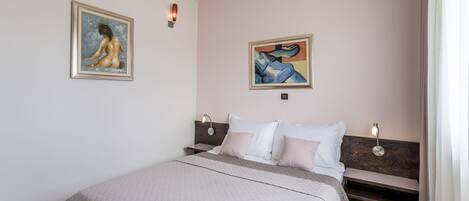 Un dormitorio con cama, dos cuadros, una mesita de noche y una lámpara de pared.