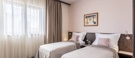 A hotel room with two beds, beige bedding, a painting on the wall, and a window with curtains.