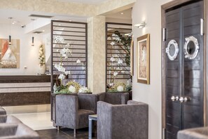 A modern reception area with a reception desk, grey seating, decorative plants, and a dark wooden door.