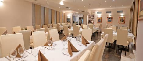 Un amplio comedor con varias mesas dispuestas para comer, con manteles blancos y cubertería impecable.