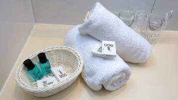 A neatly arranged bathroom with a white towel, a white bath mat, and a wicker basket containing toiletries.