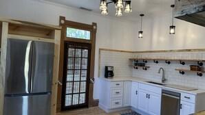 A modern kitchen with a stainless steel refrigerator, white cabinetry, a coffee maker, and a built-in dishwasher. - The Cottage @ 241 North (St. George)