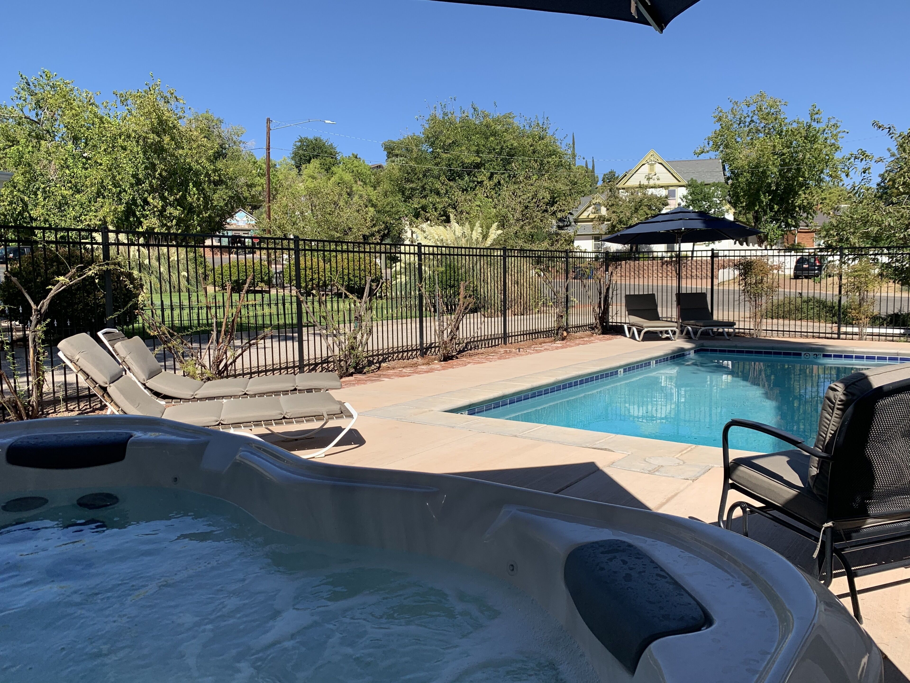 A backyard with a swimming pool, lounge chairs, and a hot tub.