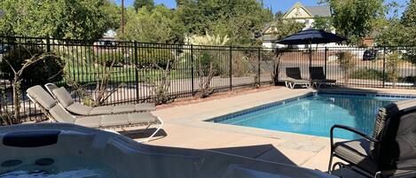 A backyard with a swimming pool, lounge chairs, and a hot tub.