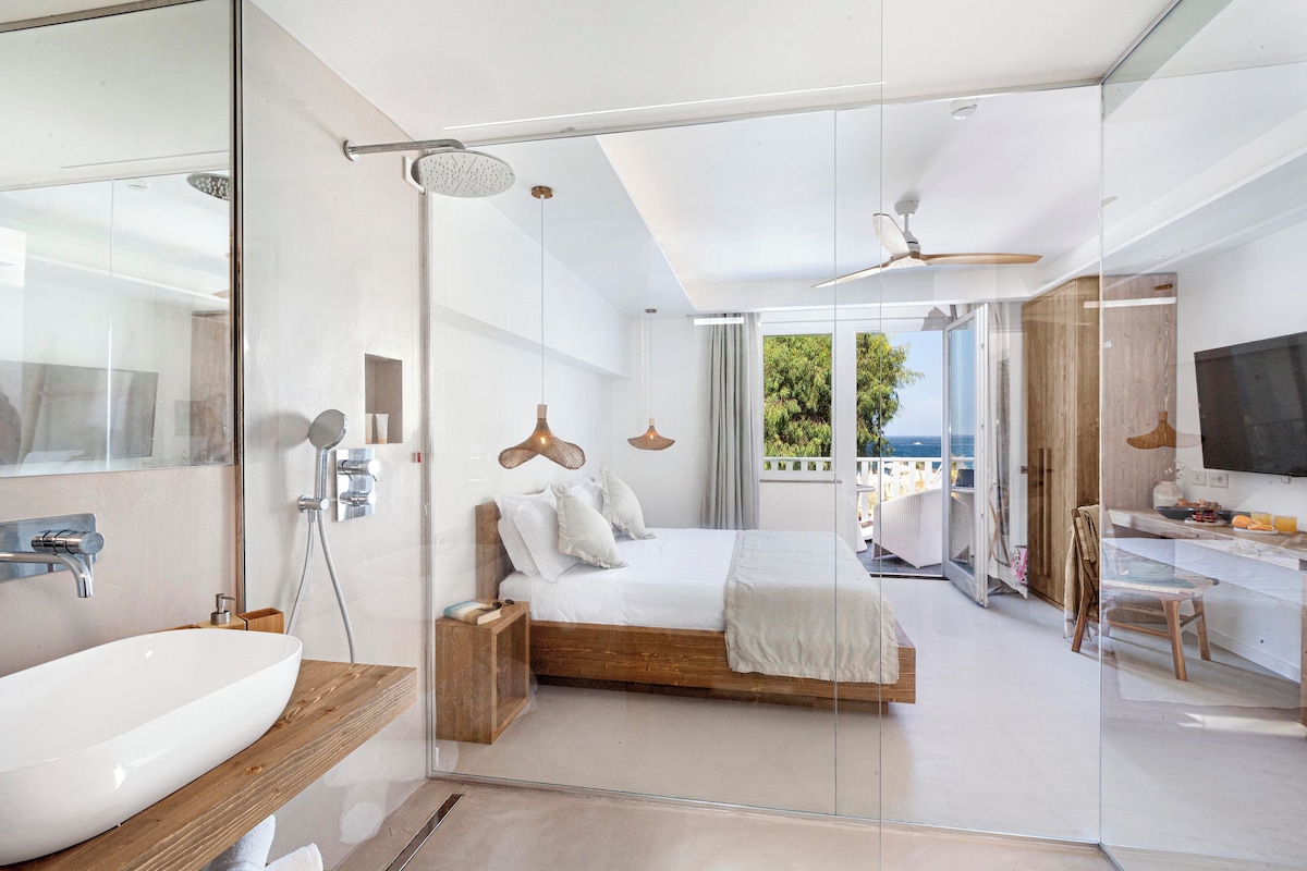 Un dormitorio moderno con ducha de vidrio, una cama grande, un televisor y un balcón con vistas.