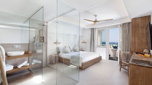 A modern hotel room with a glass-enclosed shower, a bed with white linens, a wooden desk, and a view of the sea. - Maya Beach Resort (Massa Lubrense)