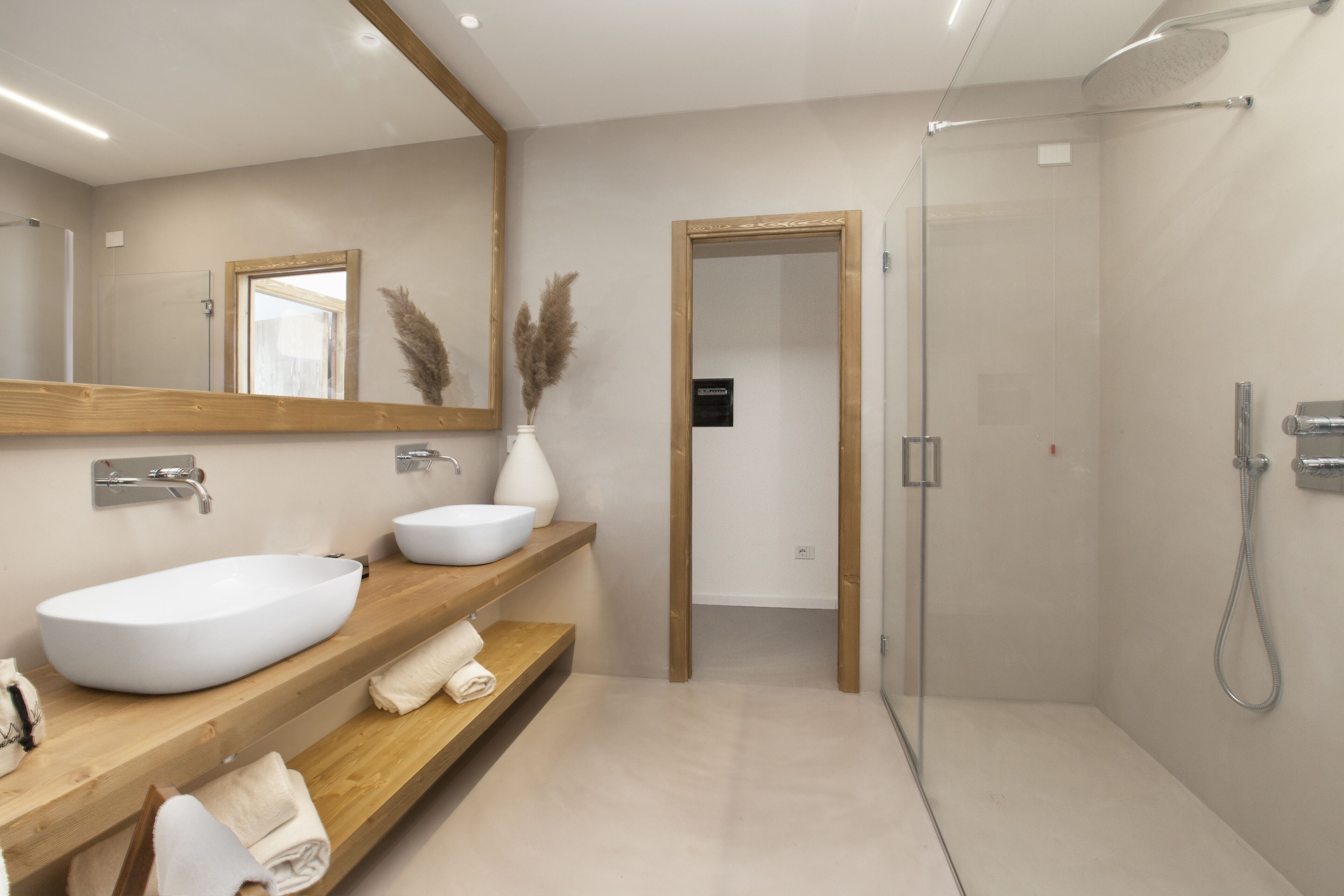 Une salle de bain moderne avec un grand lavabo sur pied, des étagères en bois, un miroir et une douche séparée par une paroi de verre.