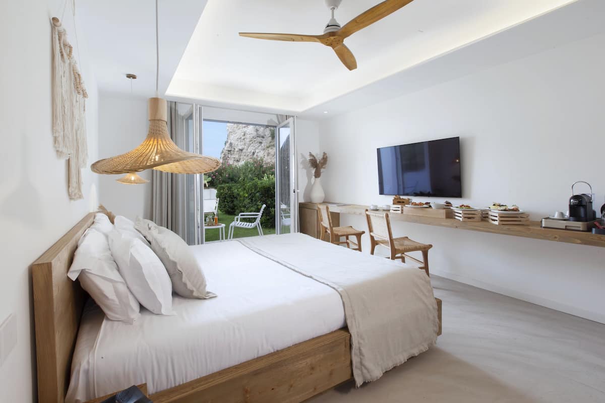 Une chambre moderne comprenant un lit, un ventilateur de plafond, un téléviseur et un coin repas avec des chaises et une table.