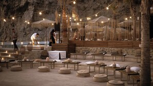 An outdoor seating area with tables and benches, string lights, and a stone wall backdrop. - Maya Beach Resort (Massa Lubrense)