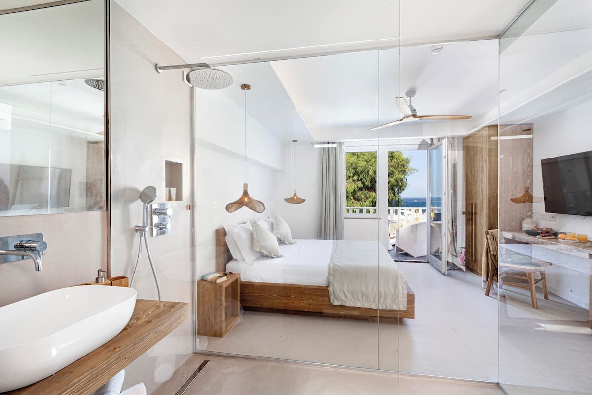 Une chambre moderne dotée d’une douche en verre, d’un grand lit, d’une télévision et d’un balcon avec vue.