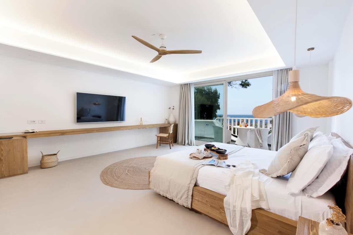 Un dormitorio moderno con una cama grande, un televisor montado en la pared, un ventilador de techo y vistas al exterior.