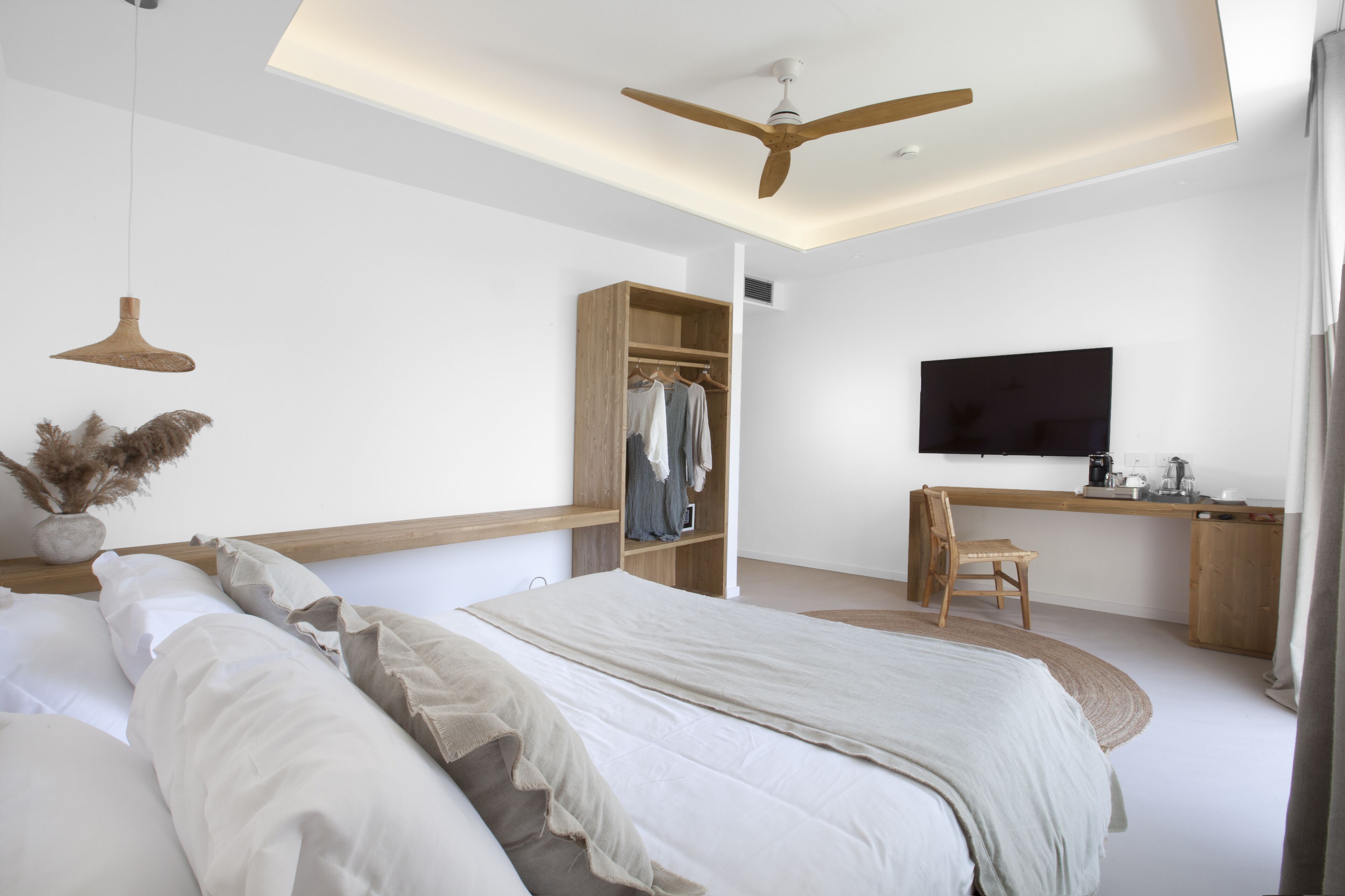 A modern bedroom with a bed, bedside table, wardrobe, desk, chair, and a television.