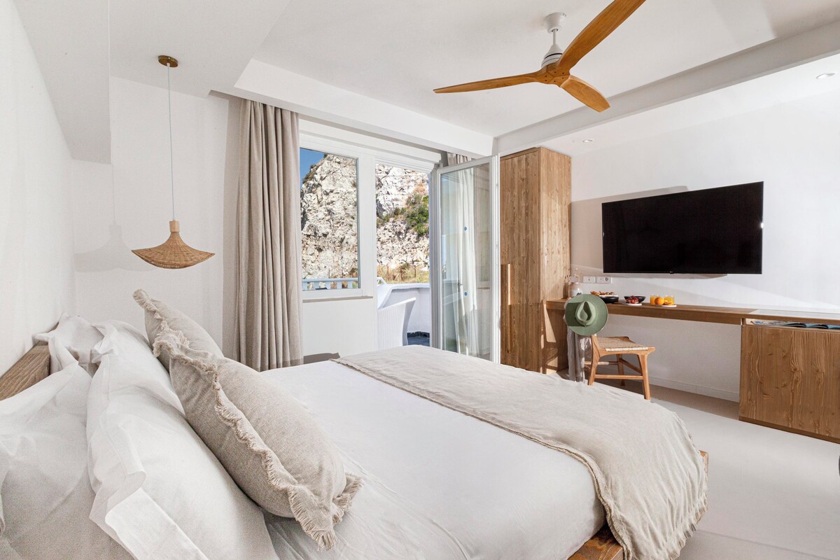 Un dormitorio con cama, escritorio, televisor y vista al exterior.