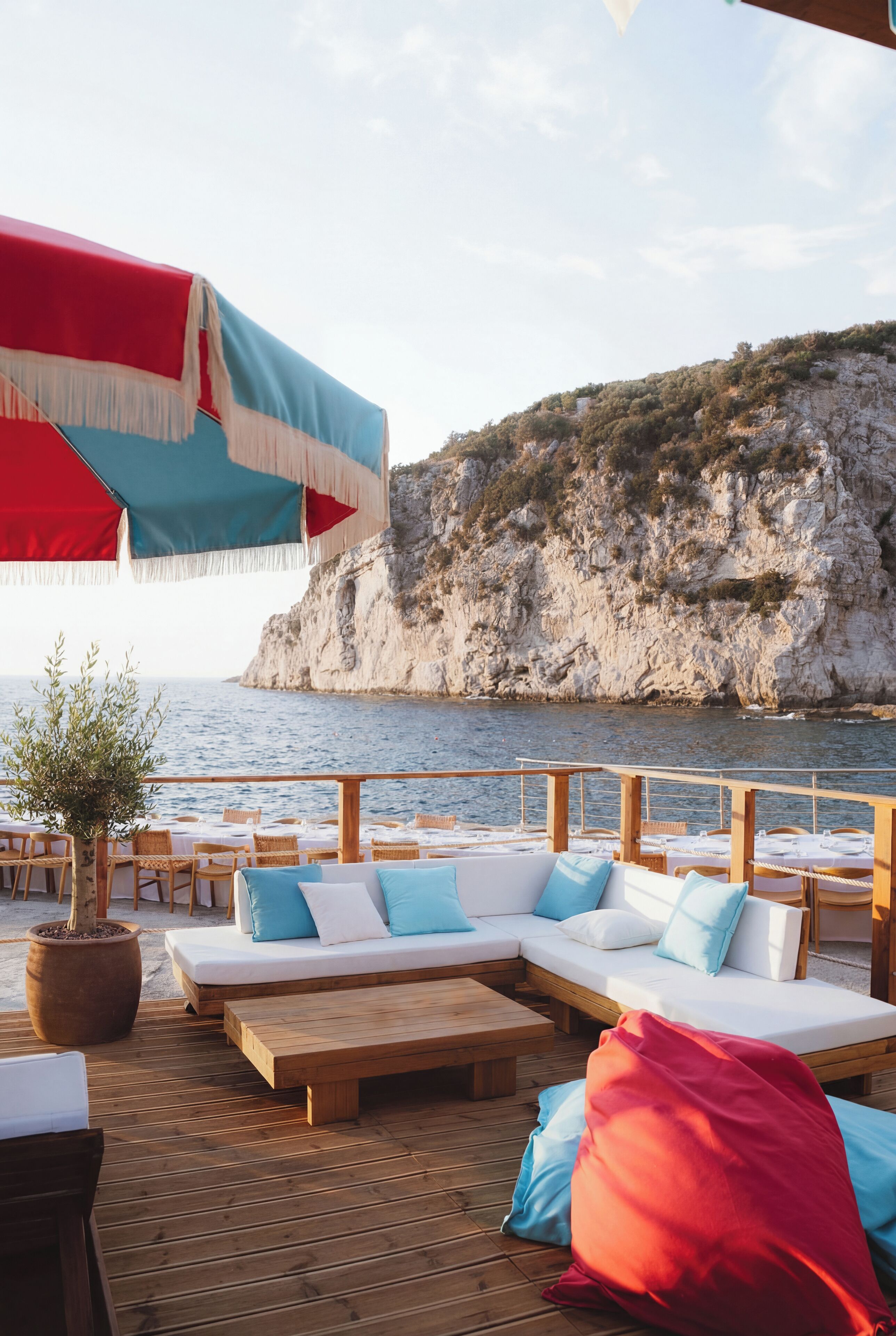 Une terrasse en bois avec des sièges d’extérieur, un grand parasol et une vue sur la mer et les falaises.