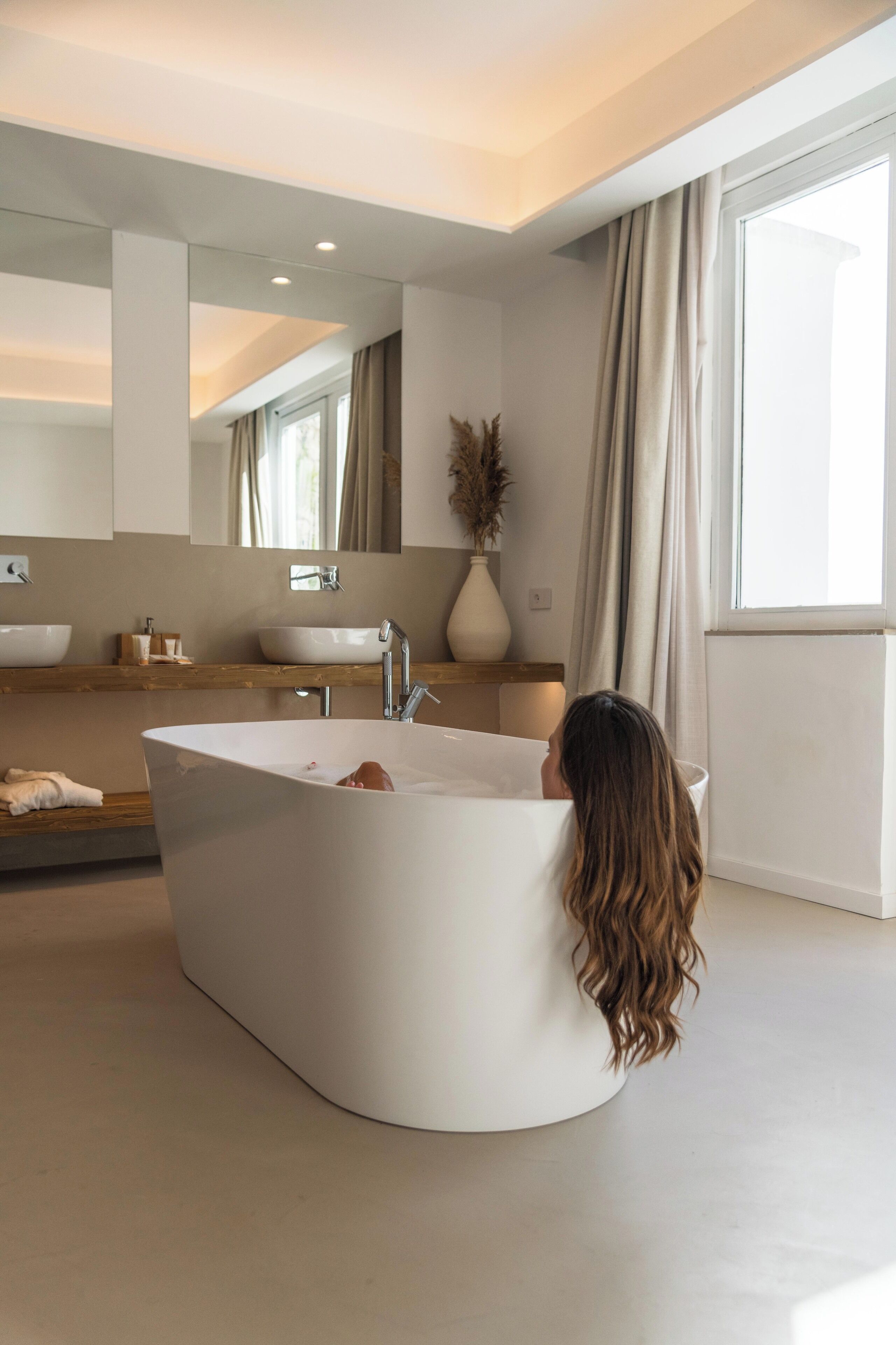 Un baño moderno con una bañera independiente, un espejo grande y una ventana con cortinas.